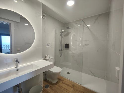 Baño moderno del hotel Nido Anaga en Tenerife con azulejos de mármol, ducha lluvia, espejo iluminado y suelo de madera
