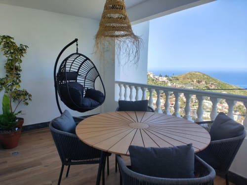 Balcón de Nido Anaga con silla colgante, mesa redonda, asientos negros y vistas panorámicas del Mediterráneo en Tenerife