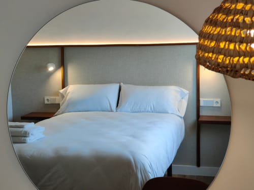 Dormitorio moderno con ropa de cama blanca en Nido Anaga, Santa Cruz de Tenerife, con espejo circular e iluminación ambiental