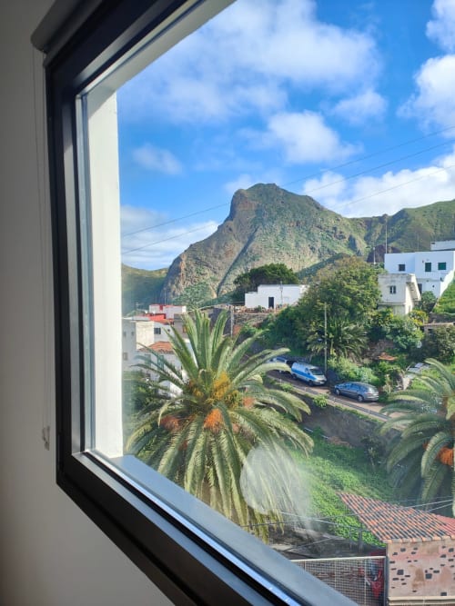 Vista desde la ventana de Nido Anaga con palmeras, montañas y pueblo costero de Santa Cruz de Tenerife, Islas Canarias