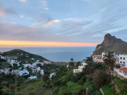 Vista del atardecer sobre la costa de Anaga con casas encaladas, palmeras y formaciones rocosas dramáticas cerca de Nido Anaga