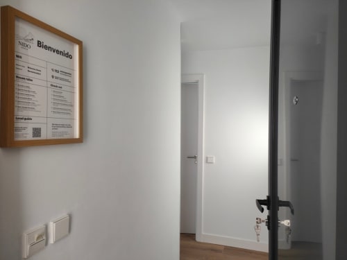 Recibidor moderno en Nido Anaga, Tenerife con letrero de bienvenida, paredes blancas, puerta de madera y diseño minimalista