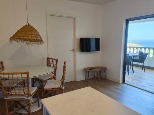 Modern apartment at Nido Anaga with dining area, woven pendant lamp, wall-mounted TV, and sea view balcony access in Santa