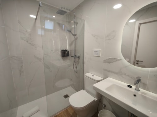 Modern bathroom with marble tiles, glass shower enclosure, white sink, and toilet at Nido Anaga, Santa Cruz de Tenerife