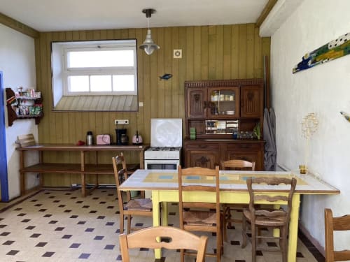 Rustic kitchen-dining area with yellow table, wooden chairs, green walls, and vintage stove at Le Lama Zébré B&B in Penmarch,