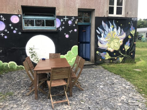 Wooden dining table and chairs on gravel patio at Le Lama Zébré B&B in Penmarch, with whimsical moon and flower wall murals