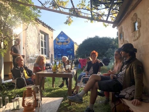 Guests socializing in the garden at Le Lama Zébré B&B in Penmarch, France, with wine and outdoor seating.