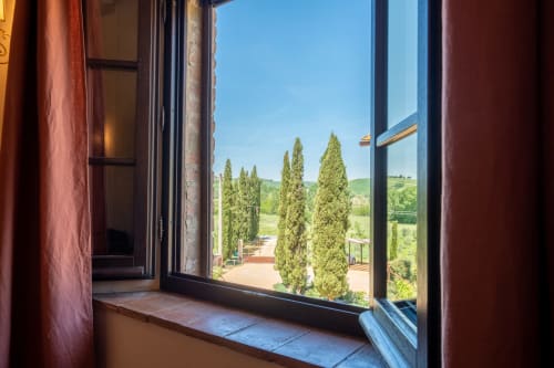 Open window view of cypress trees and rolling Tuscan hills from Agriturismo La Frattina room in Siena
