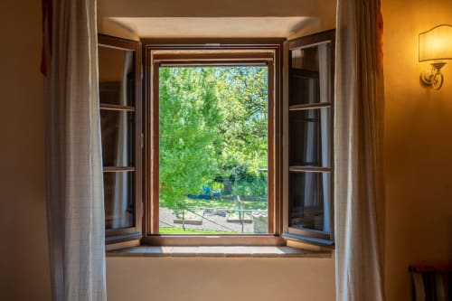 Open wooden window in Oliveta room at Agriturismo La Frattina, Buonconvento, overlooking lush garden with seating area