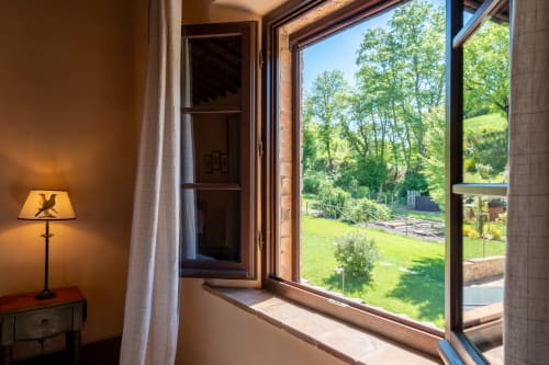 Oliveta room at Agriturismo La Frattina with open windows overlooking green garden and Tuscan countryside near Siena