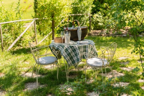 Outdoor garden dining setup at Agriturismo La Frattina in Siena with picnic basket and wine near green vineyard trellises