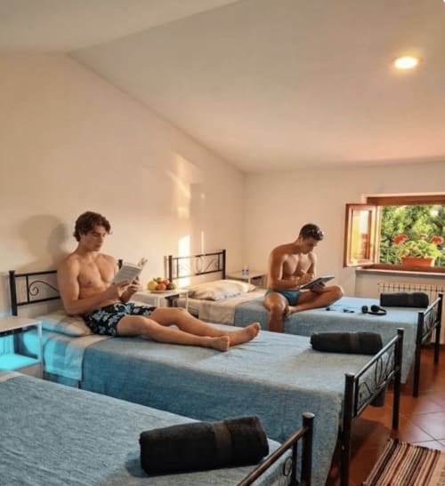 Male dorm room at B&B Rio Grande hostel in Massarosa with multiple beds, guests reading, and natural light from window