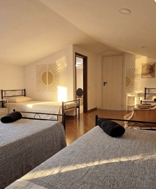Bright dormitory room at B&B Rio Grande in Massarosa with multiple beds, metal frames, and sun-themed wall decor