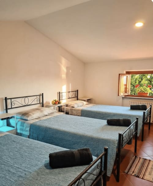 Male dormitory room at B&B Rio Grande hostel in Massarosa, featuring three beds with blue linens and metal headboards