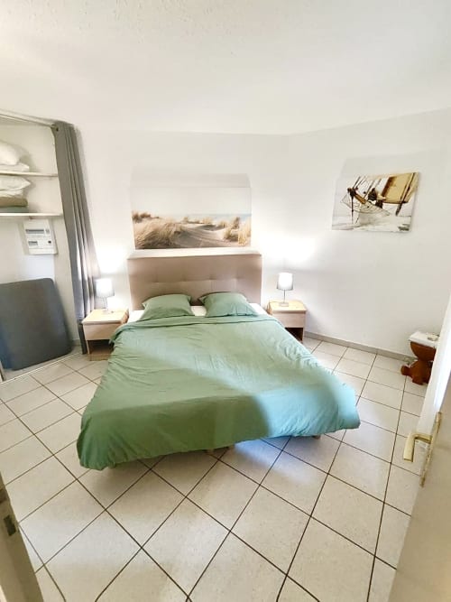 Chambre lumineuse de l'appartement Barcaresa à Port Leucate avec literie verte, tête de lit beige, carrelage et décor côtier