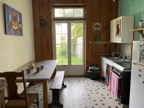 Rustic kitchen with wooden walls, dining table, and green door at Le Lama Zébré BnB in Penmarch