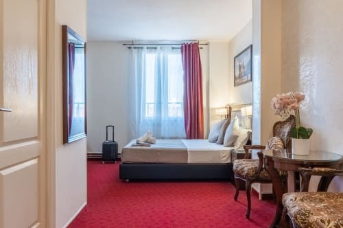 Stanza d'albergo luminosa presso l'Hotel Royal Paris Ivry con moquette rossa, letto queen, tende bordeaux e arredi classici