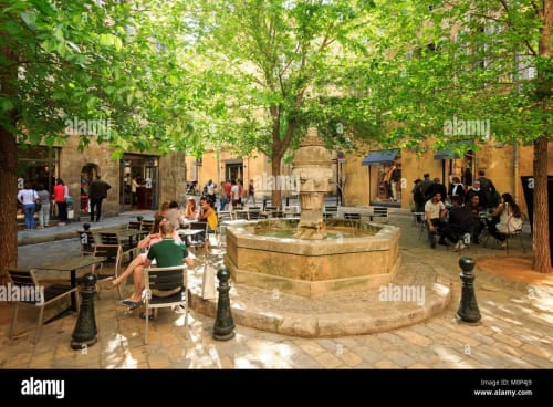 Charming courtyard at Les Suites de Montigny in Aix-en-Provence with stone fountain, shade trees, seating areas, and historic