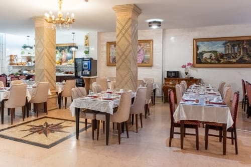 Elegantes Speisezimmer des Hotel Royal Paris Ivry mit weißen Tischdecken, gepolsterten Stühlen, klassischen Säulen und gerahmten Bildern