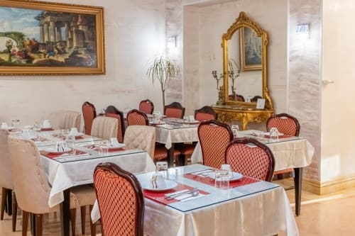 Elegantes Esszimmer des Hotel Royal Paris Ivry mit formalen Tischen, roten gemusterten Stühlen, verziertem Goldspiegel und klassischem Stil