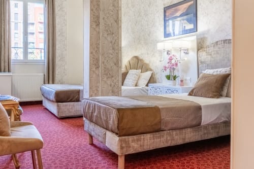 Spaziosa camera dell'Hotel Royal Paris Ivry con letti gemelli, elegante carta da parati beige, moquette rosa e zona vanity con specchio