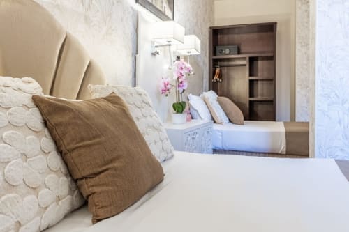 Camera da letto elegante presso l'Hotel Royal Paris Ivry con biancheria color crema, cuscini marroni e orchidee rosa sul comodino