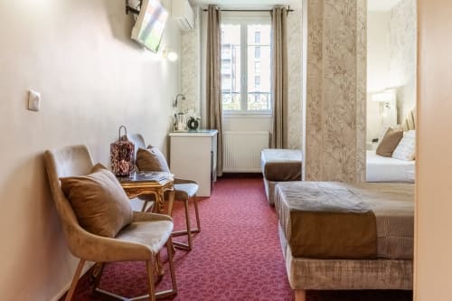 Camera spaziosa dell'Hotel Royal Paris Ivry con sedute in pelle marrone, moquette rosa e arredamento in stile parigino