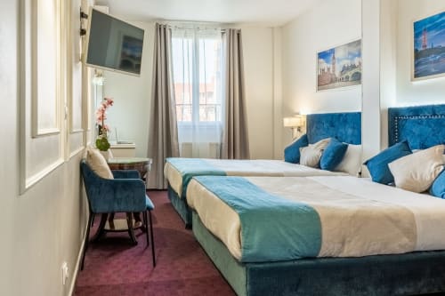 Camera d'hotel moderna presso Hotel Royal Paris Ivry con letti gemelli, testiere blu e dipinti dei monumenti parigini alle pareti