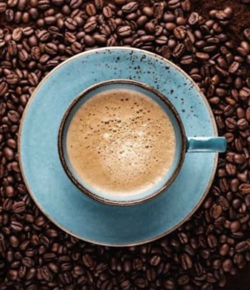 Café espresso dans une tasse en céramique bleue entourée de grains de café à l'Alombre B&B, Lectoure France