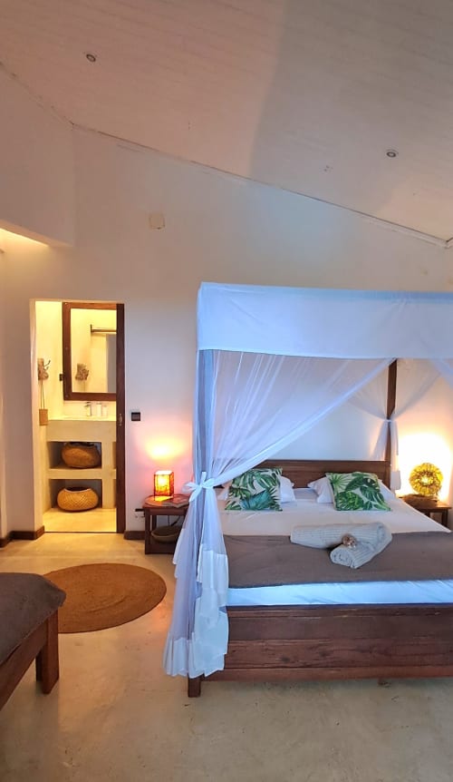 Camera da letto lussuosa a La Villa Boraha con letto a baldacchino blu, arredamento tropicale e bagno privato a Vohilava, Madagascar
