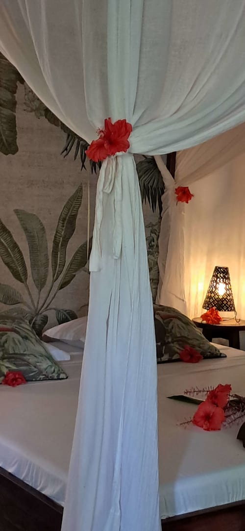 Élégant baldaquin blanc aérien orné de fleurs rouges dans une luxueuse chambre à La Villa Boraha, resort balnéaire de Vohilava