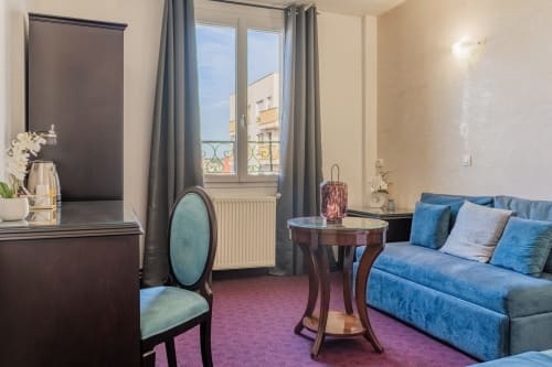 Suite elegante all'Hotel Royal Paris Ivry con divano blu, sedia menta, tavolo rotondo e vista sulle strade parigine