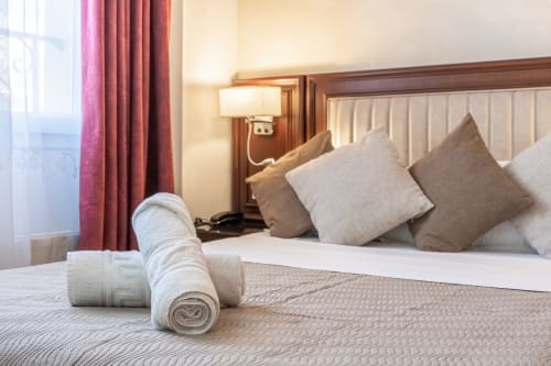 Camera dell'Hotel Royal Paris Ivry con asciugamani arrotolati sul letto, cuscini beige, tende bordeaux e lampada da comodino