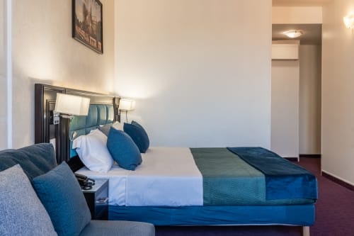 Camera dell'Hotel Royal Paris Ivry con letto imbottito blu, cuscini bianchi e illuminazione moderna a Ivry-sur-Seine