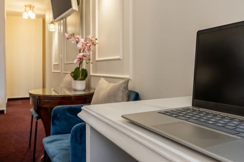 Moderno spazio di lavoro in camera d'albergo presso l'Hotel Royal Paris Ivry con laptop, orchidea rosa e poltrona in velluto blu