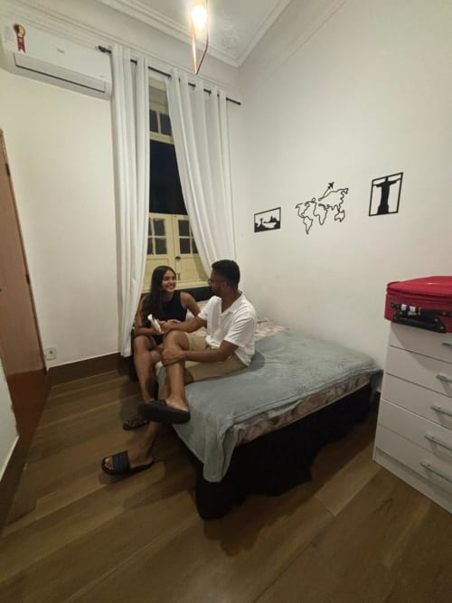 Two guests sitting on a bed in a hostel room at Rio Vibes Hostel in Rio de Janeiro, with white walls and world map decor