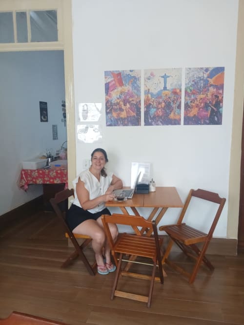 Mulher trabalhando em uma mesa de madeira no dormitório do albergue Rio Vibes no Rio de Janeiro, com obras de arte coloridas nas paredes