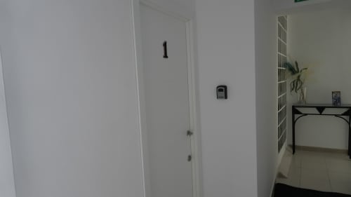 Pasillo limpio de habitación en Hostal Merino Jédula con paredes blancas, puerta, termostato y vista del dormitorio con escritorio
