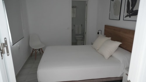 Acogedora habitación doble en el Hostal Merino Jédula con ropa de cama blanca, cabecero de madera y baño privado
