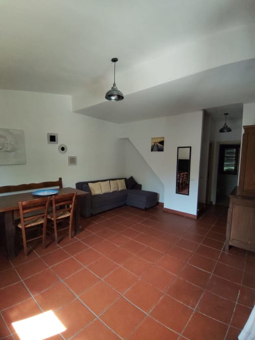 Modern living room with terracotta tile floor, dining area, dark sofa, and pendant lighting in San Teodoro holiday villa