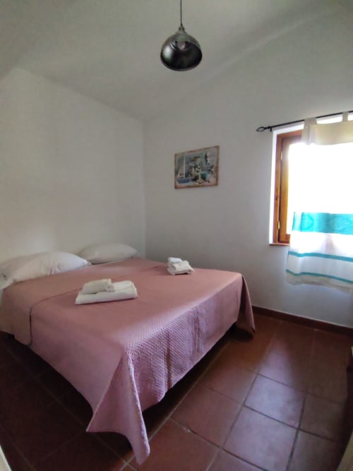 Bedroom at Oasi Villetta Adriana, San Teodoro with pink bedding, pendant lamp, and garden view window