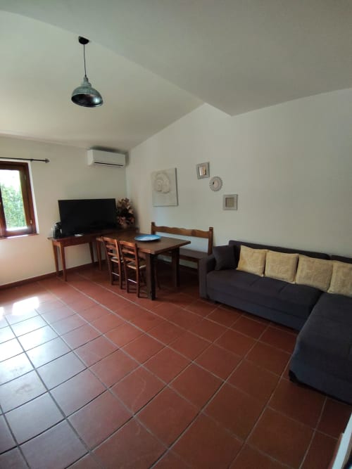 Modern living room at Oasi Villetta Adriana with black sofa, dining table, TV, terracotta flooring, and air conditioning in
