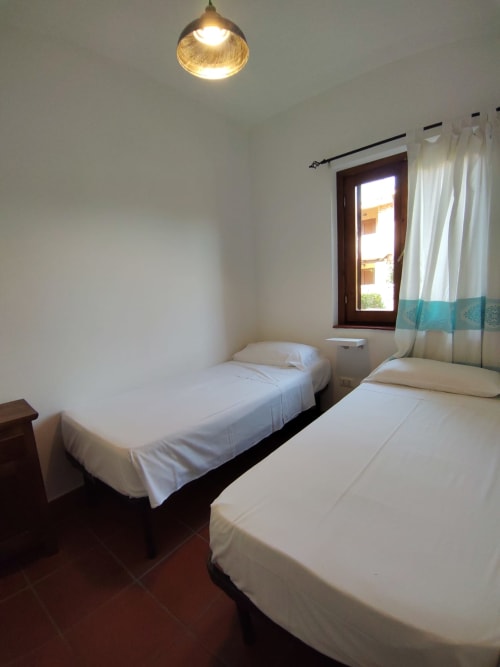 Twin bedroom in Oasi Villetta Adriana at San Teodoro with white beds, pendant light, and garden view window