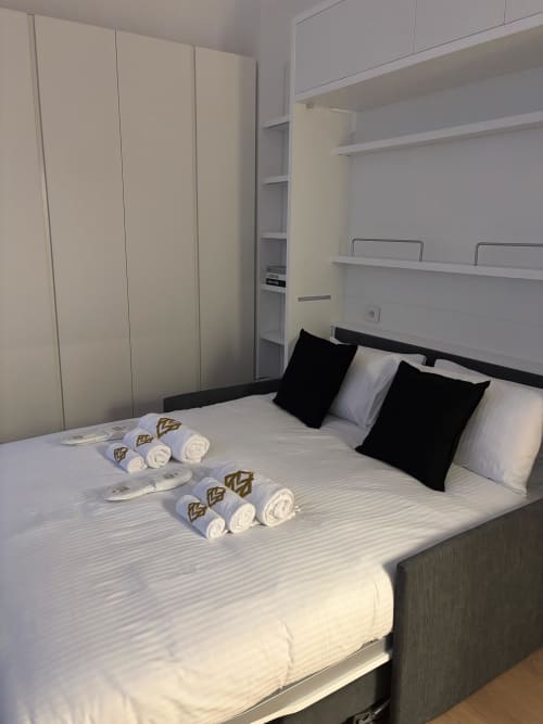 Modern bedroom at Maisons Milano with queen bed, rolled towels, black pillows, and cream wardrobe closet
