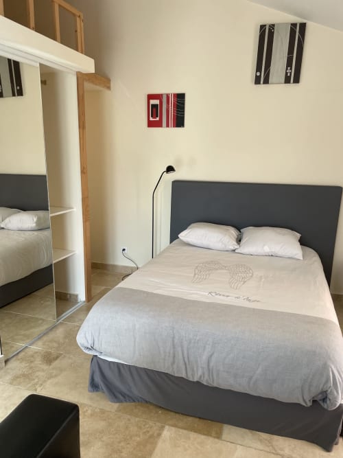 Chambre moderne à l'Hôtel d'Albion à Sault avec lit gris capitonné, draps blancs, miroir et art mural contemporain