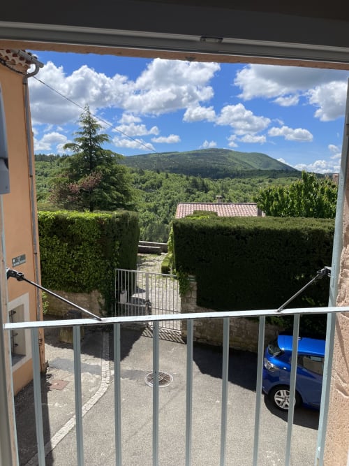 Vue sur la montagne depuis le balcon du Studio centre de Sault, Hôtel d'Albion, avec voiture bleue garée et haies vertes
