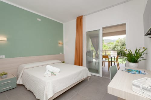 Modern bedroom at Le Dune Relax hotel in San Teodoro with mint green accent wall, white bed, and pool view balcony access