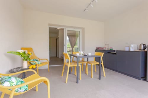 Modern lounge area at Le Dune Relax with yellow chairs, dining table, and kitchenette overlooking pool