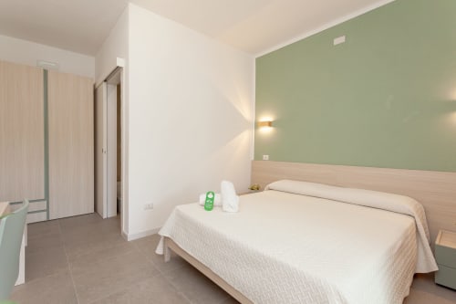 Modern bedroom at Le Dune Relax hotel in San Teodoro with queen bed, green accent wall, and pool view access