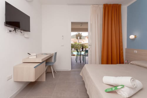 Modern hotel room at Le Dune Relax in San Teodoro with pool view, king bed, desk, flat-screen TV, and balcony access
